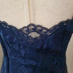 K&ouml;nnte beinhalten: Ein nachtblaues Satin-Schlafkleid mit Blumenmuster und Spitzenbesatz am Ausschnitt.