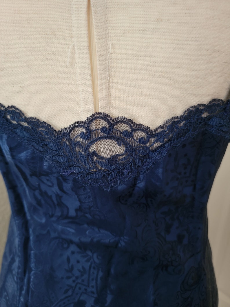 K&ouml;nnte beinhalten: Ein nachtblaues Satin-Schlafkleid mit Blumenmuster und Spitzenbesatz am Ausschnitt.