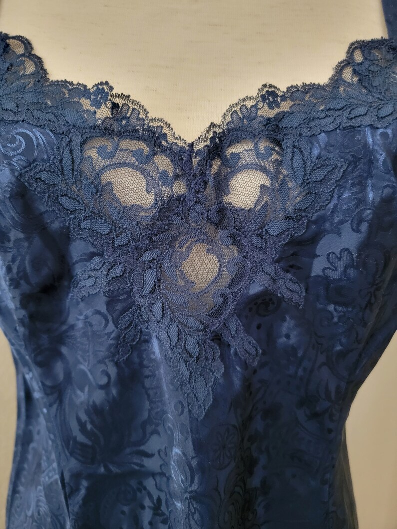 K&ouml;nnte beinhalten: Ein nachtblauer Satin-Schlafanzug mit einer Spitzenborte am Ausschnitt. Die Spitze ist ein zartes Blumenmuster.