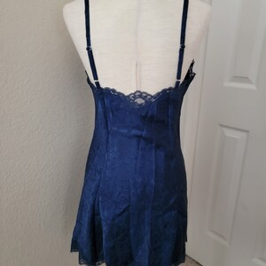 K&ouml;nnte beinhalten: Ein nachtblaues Satin-Schlafkleid mit Spitzenbesatz. Das Kleid hat einen figurbetonten Oberteil und einen flie&szlig;enden Rock.