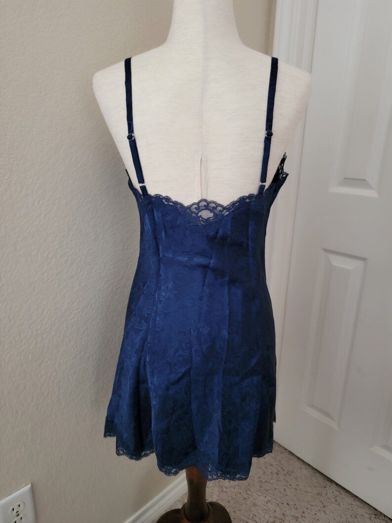 K&ouml;nnte beinhalten: Ein nachtblaues Satin-Schlafkleid mit Spitzenbesatz. Das Kleid hat einen figurbetonten Oberteil und einen flie&szlig;enden Rock.