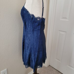 K&ouml;nnte beinhalten: Ein nachtblaues Satin-Schlafkleid mit Spitzenbesatz. Das Kleid hat einen figurbetonten Oberteil und einen flie&szlig;enden Rock.