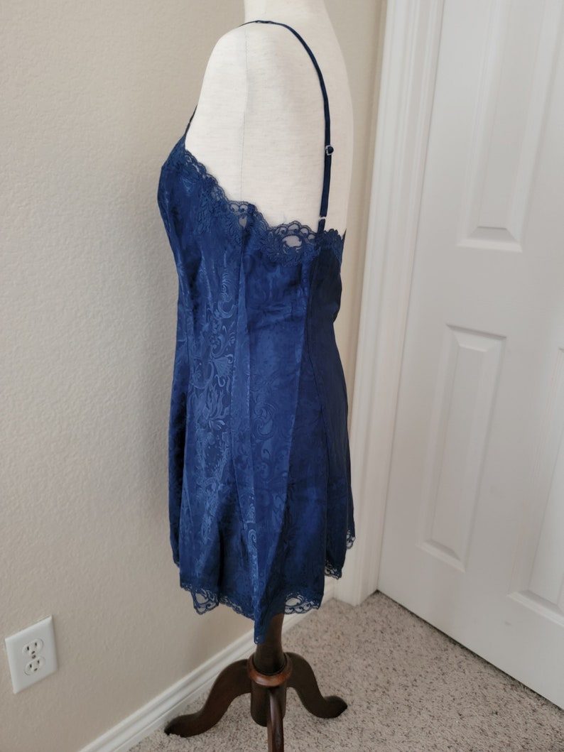 K&ouml;nnte beinhalten: Ein nachtblaues Satin-Schlafkleid mit Spitzenbesatz. Das Kleid hat einen figurbetonten Oberteil und einen flie&szlig;enden Rock.