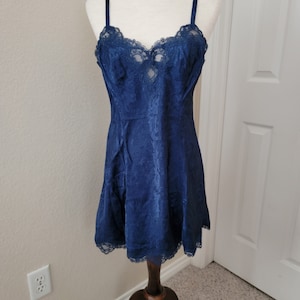 K&ouml;nnte beinhalten: Ein nachtblaues Satin-Schlafkleid mit Spitzenbesatz. Das Kleid hat ein figurbetontes Oberteil und einen flie&szlig;enden Rock.