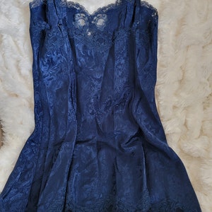 K&ouml;nnte beinhalten: Ein nachtblaues Satin-Schlafkleid mit Spitzenbesatz. Das Kleid hat ein Blumenmuster und verstellbare Tr&auml;ger.