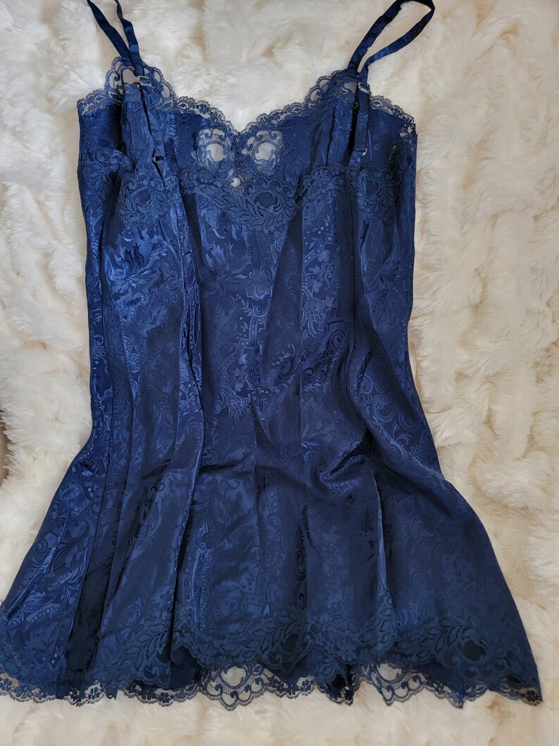 K&ouml;nnte beinhalten: Ein nachtblaues Satin-Schlafkleid mit Spitzenbesatz. Das Kleid hat ein Blumenmuster und verstellbare Tr&auml;ger.