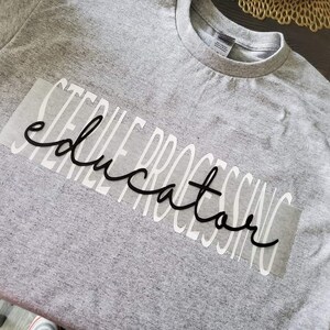 May include: A gray t-shirt with a white vinyl design that says "STEEL PROCESSING EDUCATOR".