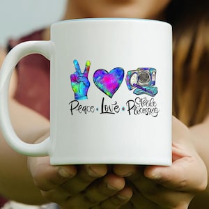 May include: White ceramic mug with a blue rim, featuring the words "Peace, Love, Sterile Processing." The design includes a peace sign, a heart, and a medical device, all in vibrant tie-dye colors. The mug is held by a person.