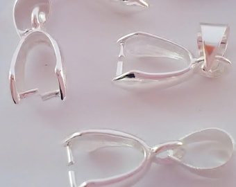 Puede incluir: Varios pequeños cierres de joyería plateados y brillantes están dispersos sobre un fondo claro. Cada cierre tiene un diseño curvo y abierto con un pequeño lazo en la parte superior para sujetar a una cadena u otro componente de joyería. Los cierres parecen ser de metal.