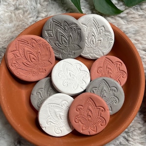 May include: A collection of eight ceramic coasters featuring a floral design in shades of grey, white, and terracotta. The coasters are arranged in a terracotta bowl.