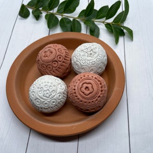 May include: Four decorative ceramic spheres with intricate patterns in shades of brown and white. The spheres are arranged on a terracotta plate.