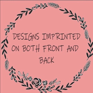 May include: A pink background with a black floral wreath design. The text in the center reads "DESIGNS IMPRINTED ON BOTH FRONT AND BACK". The wreath is composed of leaves, flowers, and other botanical elements.