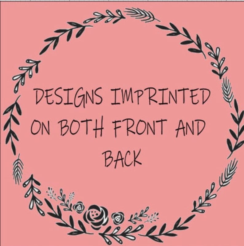 May include: A pink background with a black floral wreath design. The text in the center reads "DESIGNS IMPRINTED ON BOTH FRONT AND BACK". The wreath is composed of leaves, flowers, and other botanical elements.
