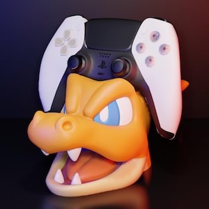 Peut inclure: Un support de manette sur le thème de Charizard, orange vif, avec une manette PlayStation 5 noire et blanche posée dessus. Le support présente une tête de dragon détaillée avec des yeux bleus et des dents pointues.