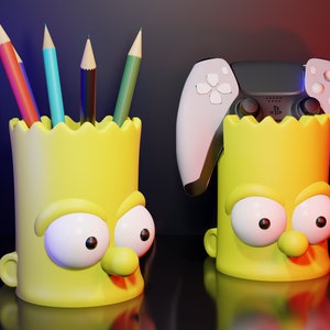 May include: Two yellow Simpsons character pencil holders. One holder has a black and white PlayStation 5 controller on top. The other holder has five colored pencils inside.