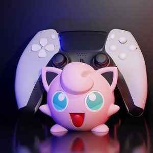 May include: A white and black PlayStation 5 DualSense controller with a pink and white Jigglypuff plush toy in front of it.