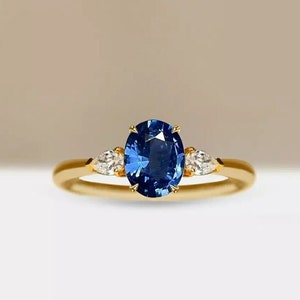 Könnte beinhalten: Ein goldener Ring mit einem großen ovalen blauen Saphir und zwei kleineren birnenförmigen Diamanten auf jeder Seite.