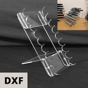 Puede incluir: Un portaplumas de acrílico transparente con 12 ranuras para bolígrafos. El soporte está inclinado y tiene una base para estabilidad. El soporte se muestra con bolígrafos en las ranuras.