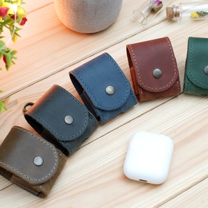 May include: Five leather cases for wireless earbuds in different colors: brown, dark blue, light blue, green, and dark brown. The cases have a snap closure and a small metal loop.