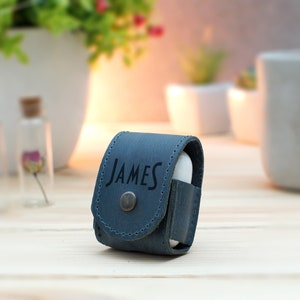 May include: A blue leather case for wireless earbuds with the name "JAMES" embossed on the front.