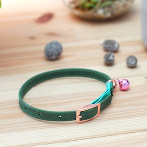 May include: A green leather cat collar with a rose gold buckle and a pink bell.