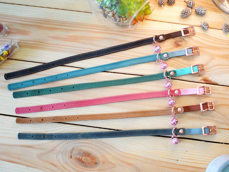 May include: Seven leather cat collars in various colors, including black, teal, green, pink, brown, and gray. Each collar has a small bell charm.