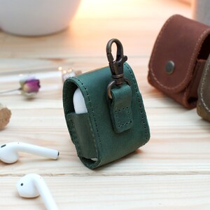 May include: Green leather case with a metal clasp for AirPods. The case has a strap for attaching to a keychain.