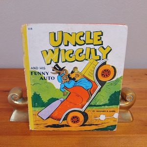 May include: A vintage children's book cover featuring Uncle Wiggily and his funny auto. The cover is illustrated with a cartoon of Uncle Wiggily driving a car with a rabbit passenger. The book is titled "Uncle Wiggily and His Funny Auto" by Howard R. Garis.