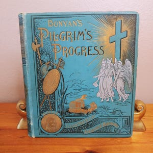 May include: A vintage, blue hardback book titled "Bunyans Pilgrim's Progress" with gold lettering and illustrations. The cover features a cross, angels, and a scene from the story.