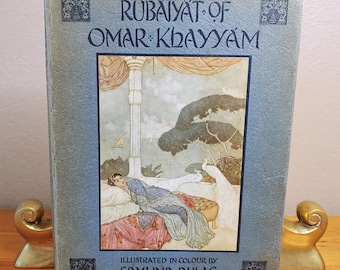 Könnte beinhalten: Ein Vintage-Buch mit dem Titel "Rubaiyat of Omar Khayyam" mit einer Illustration einer Frau, die auf einem Sofa liegt, mit Pfauen im Hintergrund. Das Buch ist von Edmund Dulac farbig illustriert.