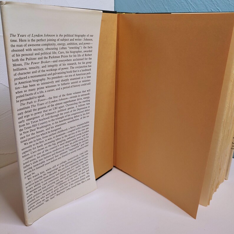 May include: An open book with text titled "The Years of Lyndon Johnson" is displayed. The book has a tan cover and gold-colored page edges. The text describes the political biography of Lyndon B. Johnson.