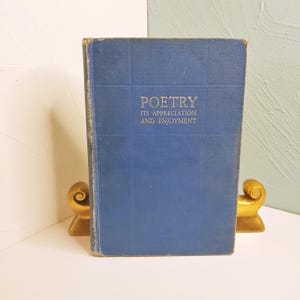May include: A vintage book titled "POETRY ITS APPRECIATION AND ENJOYMENT" with a blue cover. The book is held between two gold-colored decorative bookends. The book's cover has a grid pattern and the title is in silver lettering.