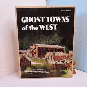 May include: A vintage book titled "Ghost Towns of the West" with a black cover and a photograph of old wooden buildings. The book is a pictorial guide to towns and mining camps. The book is a Sunset Pictorial.