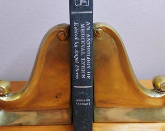 May include: A black book titled "An Anthology of Medieval Lyrics" edited by Angel Flores, standing between two brass-colored bookends. The book is from the Modern Library series.