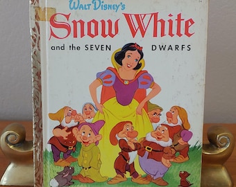 Puede incluir: Un libro vintage de Little Golden Book con Blancanieves y los Siete Enanitos de Walt Disney. La portada muestra a Blancanieves con su vestido amarillo y su capa roja, rodeada de los siete enanitos.