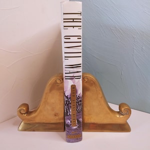 May include: A book titled "The Civil War" stands upright between two gold-colored bookends. The book's spine displays the title in large, vertical white letters. The bookends have a curved, ornate design.