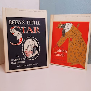 May include: Two vintage children's books. The first, "Betsy's Little Star" by Carolyn Haywood, features a dark blue cover with a white border and illustrations. The second, "The Golden Touch," has a red cover with a gold illustration of a king.