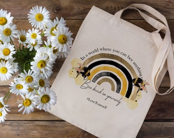 May include: A white tote bag with a rainbow and bee design. The text on the bag reads "In a world where you can be anything, Be kind to yourself #LoveYourself".