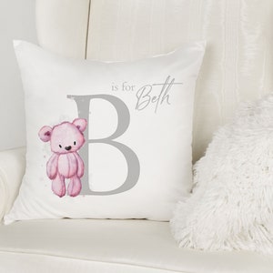 May include: A white pillow with a gray letter B and a pink teddy bear illustration. The text "is for Beth" is written in gray above the letter B.
