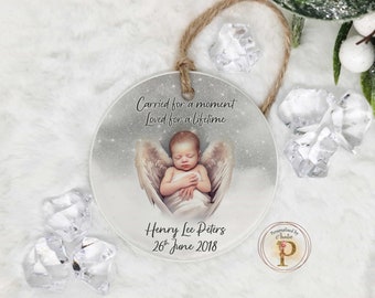 May include: A round, clear glass ornament with a white background and a baby with angel wings sleeping. The ornament has the text "Carried for a moment Loved for a lifetime" at the top, "Henry Lee Peters 26th June 2018" in the center, and "Personalised by Chentic P" at the bottom.