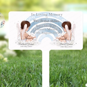 Può includere: Una targa commemorativa bianca con un arcobaleno blu e bianco e due angeli. Il testo recita "In memoria amorevole dei nostri bambini perfetti Nati dormendo Per sempre mancati 27 agosto 2022" con i nomi "Racheal Grouse 18 maggio 2023" e "David Grouse 19 maggio 2023".