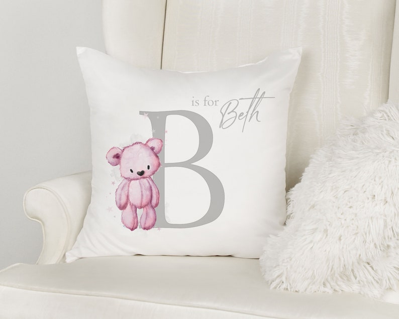 May include: A white pillow with a gray letter B and a pink teddy bear illustration. The text "is for Beth" is written in gray above the letter B.