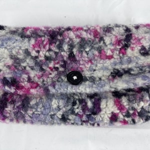 May include: A small, crocheted clutch purse with a black button closure. The purse is made with a variety of colors, including pink, purple, gray, and white.