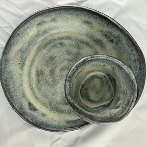 Bowl within a bowl, hand thrown, cut and rejoined. Chocolate brown with creams, purple, and blue glossy glaze. 9x9x3”. Inner bowl 4x4x3”