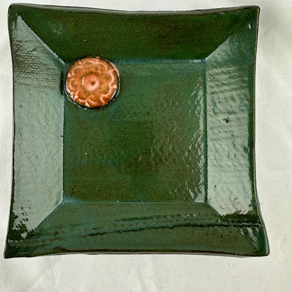 Small square plate, chocolate brown clay, sweater imprints and clay buttons. Irridescent green, pink button. 4x4x.5”