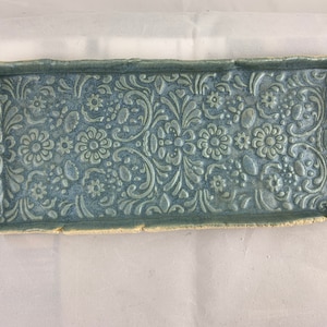 May include: A rectangular ceramic serving tray with a light blue glaze and a raised floral design.