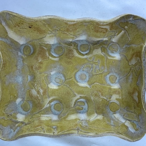 Puede incluir: Un plato de cerámica amarillo con un borde ondulado y un esmalte moteado. El plato tiene un diseño único con círculos blancos y líneas en todo.