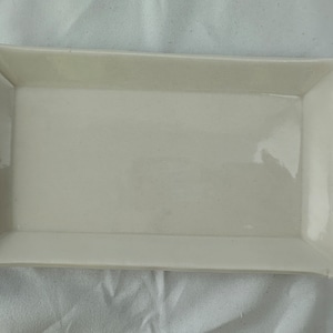 Może przedstawiać: Biała ceramiczna prostokątna taca do serwowania z lekko zakrzywionymi krawędziami.