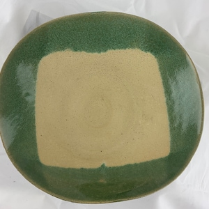 May include: A round ceramic plate with a green rim and a beige center. The plate has a square shape in the center.