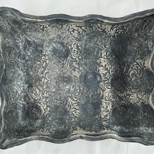 Puede incluir: Una bandeja decorativa gris con un diseño floral en relieve. La bandeja tiene un borde ondulado y está hecha de un material texturizado.